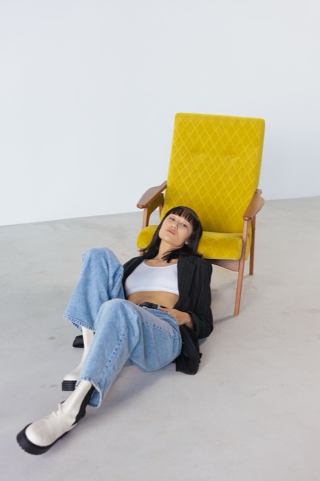 Leaning against a yellow armchair in a black blazer and jeans