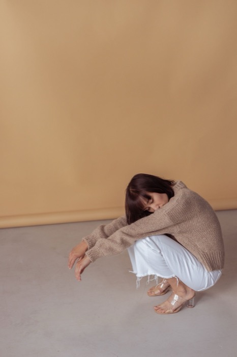 Curled up on the floor in a beige knit and white trousers