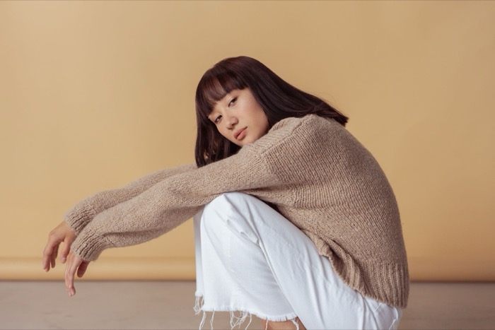 Beige jumper and white jeans, seated in profile